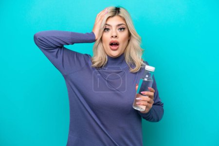 Téléchargez les photos : Jeune femme russe avec une bouteille d'eau isolée sur fond bleu avec expression surprise - en image libre de droit