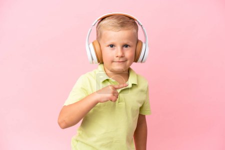 Téléchargez les photos : Petit garçon russe isolé sur fond rose écoutant de la musique et faisant un geste de guitare - en image libre de droit