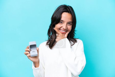 Téléchargez les photos : Jeune femme hispanique tenant une bague de fiançailles isolée sur fond bleu heureux et souriant - en image libre de droit