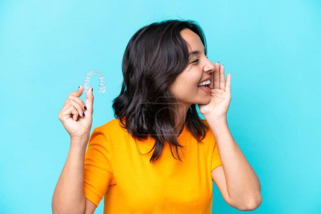 Photo for Young hispanic woman holding invisible braces isolated on blue background shouting with mouth wide open to the side - Royalty Free Image