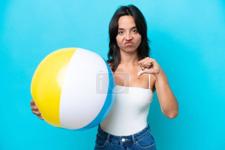 Téléchargez les photos : Jeune femme hispanique tenant ballon de plage isolé sur fond bleu montrant pouce vers le bas avec expression négative - en image libre de droit