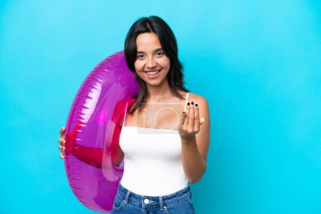 Foto de Mujer hispana joven sosteniendo donut colchón de aire aislado sobre fondo azul invitando a venir con la mano. Feliz de que hayas venido. - Imagen libre de derechos