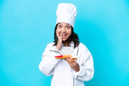 Photo for Young hispanic chef woman holding sashimi isolated on blue background with surprise and shocked facial expression - Royalty Free Image