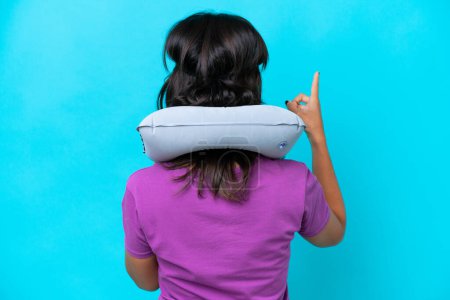Téléchargez les photos : Jeune femme caucasienne avec oreiller de voyage gonflable isolé sur fond bleu pointant vers l'arrière avec l'index - en image libre de droit