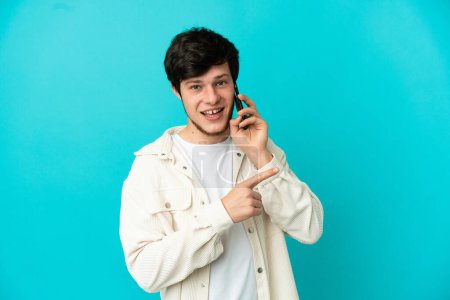 Photo for Young Russian man using mobile phone isolated on blue background pointing to the side to present a product - Royalty Free Image