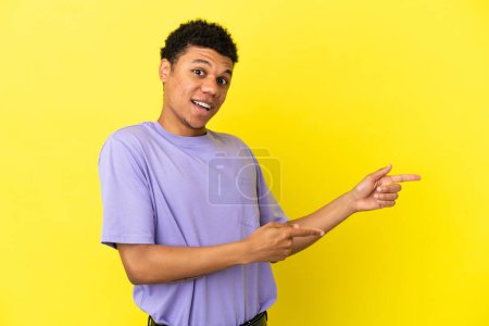 Foto de Joven afroamericano aislado sobre fondo amarillo sorprendido y apuntando lado - Imagen libre de derechos