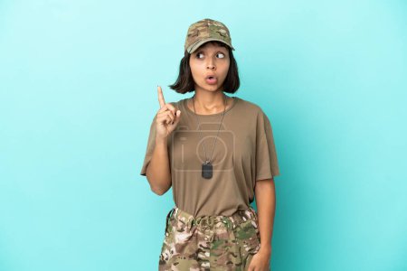 Foto de Militar mujer de raza mixta con etiqueta de perro aislado sobre fondo azul pensando en una idea apuntando con el dedo hacia arriba - Imagen libre de derechos