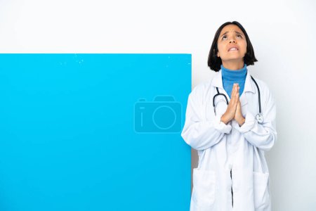 Photo for Young mixed race doctor woman with a big placard isolated on white background keeps palm together. Person asks for something - Royalty Free Image