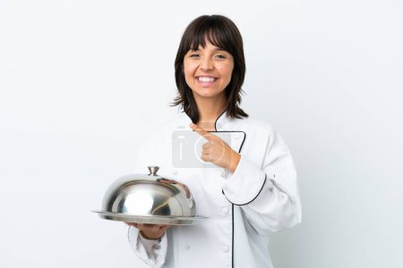 Foto de Joven chef con bandeja aislada sobre fondo blanco apuntando hacia un lado para presentar un producto - Imagen libre de derechos