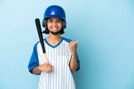 Téléchargez les photos : Baseball mixte femme joueuse avec casque et chauve-souris isolé sur fond bleu pointant vers le côté pour présenter un produit - en image libre de droit