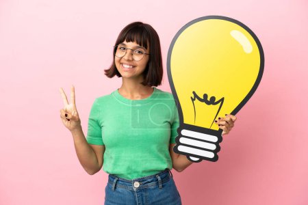 Téléchargez les photos : Jeune femme tenant une icône d'ampoule et célébrant une victoire - en image libre de droit