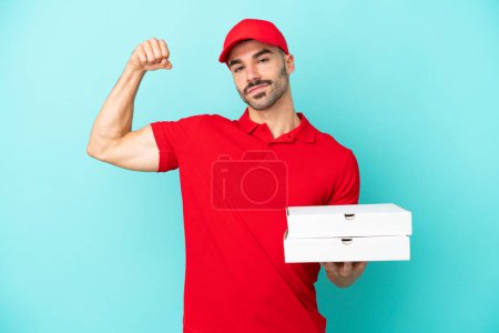 Foto de Entrega hombre caucásico recogiendo cajas de pizza aislado sobre fondo azul haciendo gesto fuerte - Imagen libre de derechos