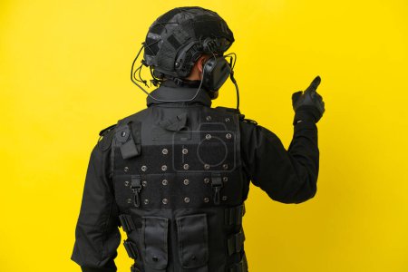 Foto de SWAT hombre caucásico aislado sobre fondo amarillo apuntando hacia atrás con el dedo índice - Imagen libre de derechos
