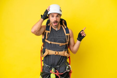 Photo for Young caucasian rock climber man isolated on yellow background surprised and pointing finger to the side - Royalty Free Image