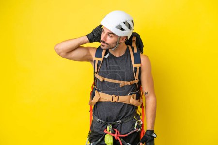 Téléchargez les photos : Jeune alpiniste caucasien isolé sur fond jaune écoutant quelque chose en mettant la main sur l'oreille - en image libre de droit