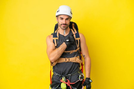 Foto de Joven escalador caucásico aislado sobre fondo amarillo apuntando hacia un lado para presentar un producto - Imagen libre de derechos