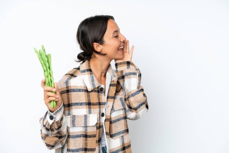 Photo for Young hispanic woman holding a green beans isolated on white background shouting with mouth wide open to the side - Royalty Free Image