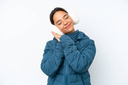 Foto de Mujer hispana joven con orejeras de invierno aisladas sobre fondo blanco haciendo gesto de sueño en expresión dorable - Imagen libre de derechos