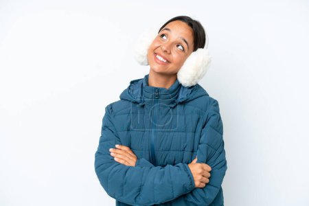 Photo for Young hispanic woman wearing a winter earmuffs isolated on white background looking up while smiling - Royalty Free Image