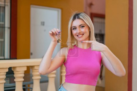 Téléchargez les photos : Jeune jolie femme blonde tenant les clés de la maison à l'extérieur et le pointant - en image libre de droit