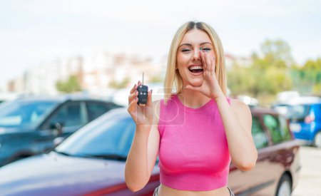 Téléchargez les photos : Jeune jolie femme blonde tenant des clés de voiture à l'extérieur criant avec la bouche grande ouverte - en image libre de droit