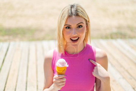 Foto de Joven mujer rubia bonita con un helado de corneta al aire libre con expresión facial sorpresa - Imagen libre de derechos