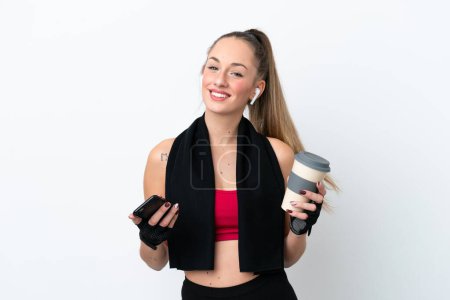 Téléchargez les photos : Jeune femme caucasienne sportive isolée sur fond blanc tenant du café à emporter et un mobile - en image libre de droit