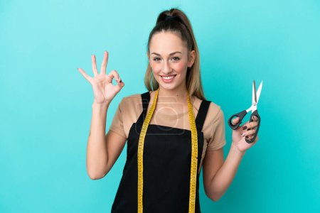 Photo for Young caucasian seamstress woman isolated on blue background showing ok sign with fingers - Royalty Free Image