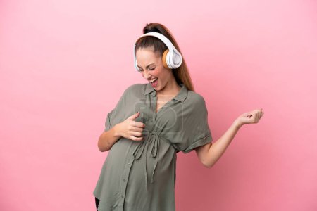 Foto de Mujer joven aislada sobre fondo rosa embarazada y escuchando música - Imagen libre de derechos