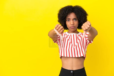 Téléchargez les photos : Jeune femme afro-américaine isolée sur fond jaune montrant pouce vers le bas avec deux mains - en image libre de droit
