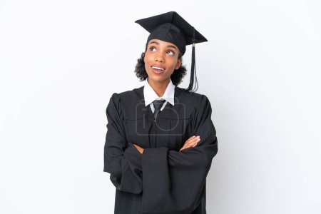 Foto de Joven graduada universitaria afroamericana aislada sobre fondo blanco mirando hacia arriba mientras sonríe - Imagen libre de derechos
