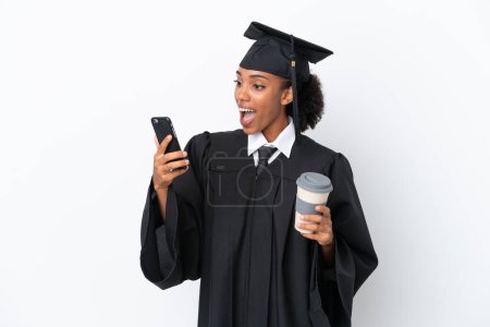 Photo for Young university graduate African American woman isolated on white background holding coffee to take away and a mobile - Royalty Free Image