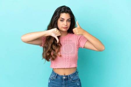 Photo for Young caucasian woman isolated on blue background making good-bad sign. Undecided between yes or not - Royalty Free Image