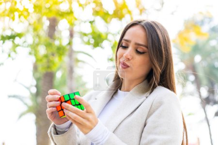 Foto de Joven mujer bonita sosteniendo un cubo de rompecabezas tridimensional al aire libre - Imagen libre de derechos