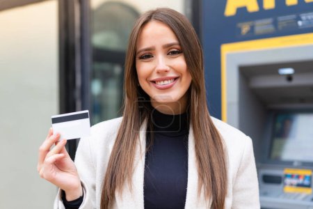 Téléchargez les photos : Jeune jolie femme tenant une carte de crédit en plein air souriant beaucoup - en image libre de droit