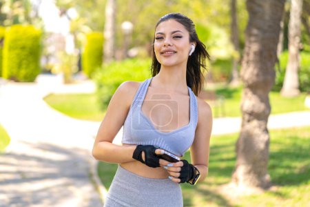 Téléchargez les photos : Jeune jolie femme en plein air portant des vêtements de sport et écoutant de la musique avec téléphone - en image libre de droit