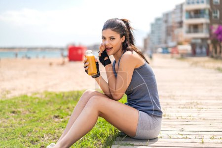 Téléchargez les photos : Jeune jolie femme sportive tenant un jus d'orange à l'extérieur chuchotant quelque chose - en image libre de droit