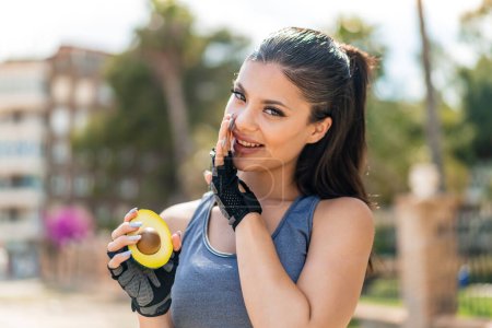 Photo for Young pretty sport woman holding an avocado at outdoors whispering something - Royalty Free Image
