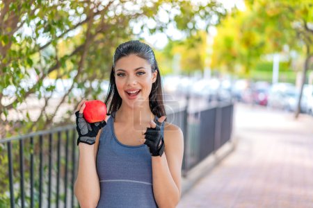 Téléchargez les photos : Jeune jolie femme sportive avec une pomme à l'extérieur surpris et pointant devant - en image libre de droit