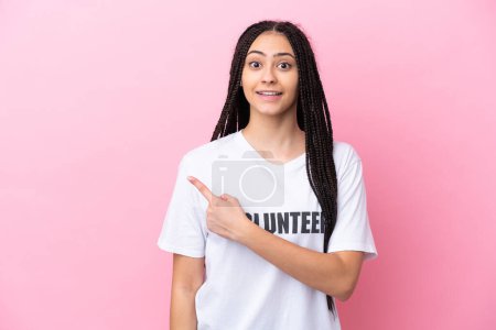Photo for Teenager volunteer girl with braids isolated on pink background pointing to the side to present a product - Royalty Free Image
