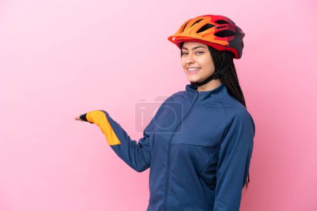 Téléchargez les photos : Adolescente cycliste fille isolé sur fond rose étendant les mains sur le côté pour inviter à venir - en image libre de droit