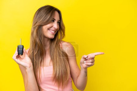 Photo for Young caucasian woman holding car keys isolated on yellow background pointing to the side to present a product - Royalty Free Image