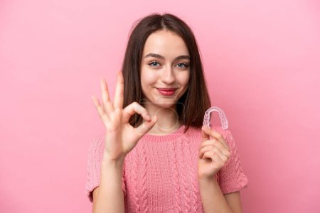 Photo for Young Ukrainian woman holding invisible braces isolated on pink background showing ok sign with fingers - Royalty Free Image