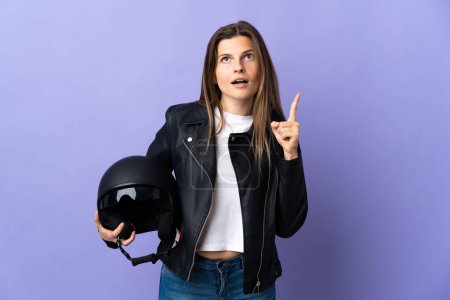 Foto de Joven eslovaca sosteniendo un casco de moto aislado sobre fondo púrpura pensando en una idea apuntando con el dedo hacia arriba - Imagen libre de derechos