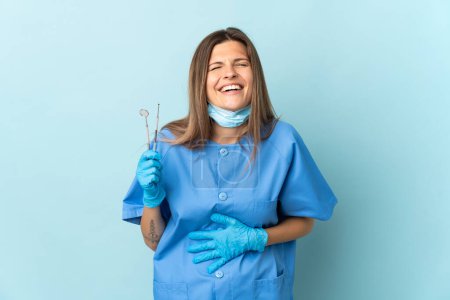 Téléchargez les photos : Dentiste slovaque tenant des outils isolés sur fond bleu souriant beaucoup - en image libre de droit