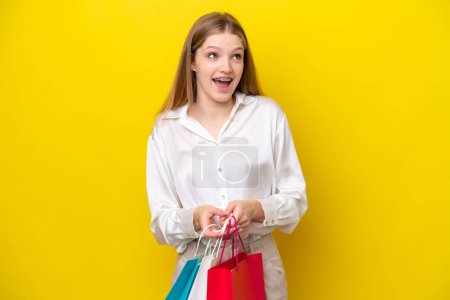 Photo for Teenager Russian girl isolated on yellow background holding shopping bags and surprised - Royalty Free Image