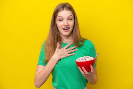 Foto de Adolescente rusa chica sosteniendo tazón de cereales aislado sobre fondo amarillo sorprendido y sorprendido mientras mira a la derecha - Imagen libre de derechos