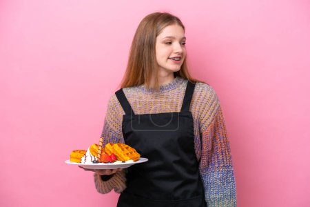Photo for Teenager Russian girl holding a waffles isolated on pink background looking to the side and smiling - Royalty Free Image