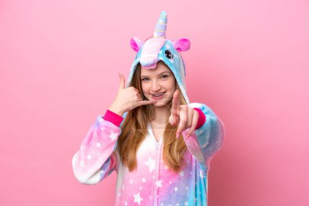Foto de Adolescente chica rusa con pijama de unicornio aislado sobre fondo rosa haciendo gesto de teléfono y apuntando hacia delante - Imagen libre de derechos