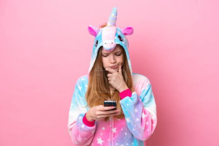 Foto de Adolescente chica rusa con pijama de unicornio aislado sobre fondo rosa pensando y enviando un mensaje - Imagen libre de derechos